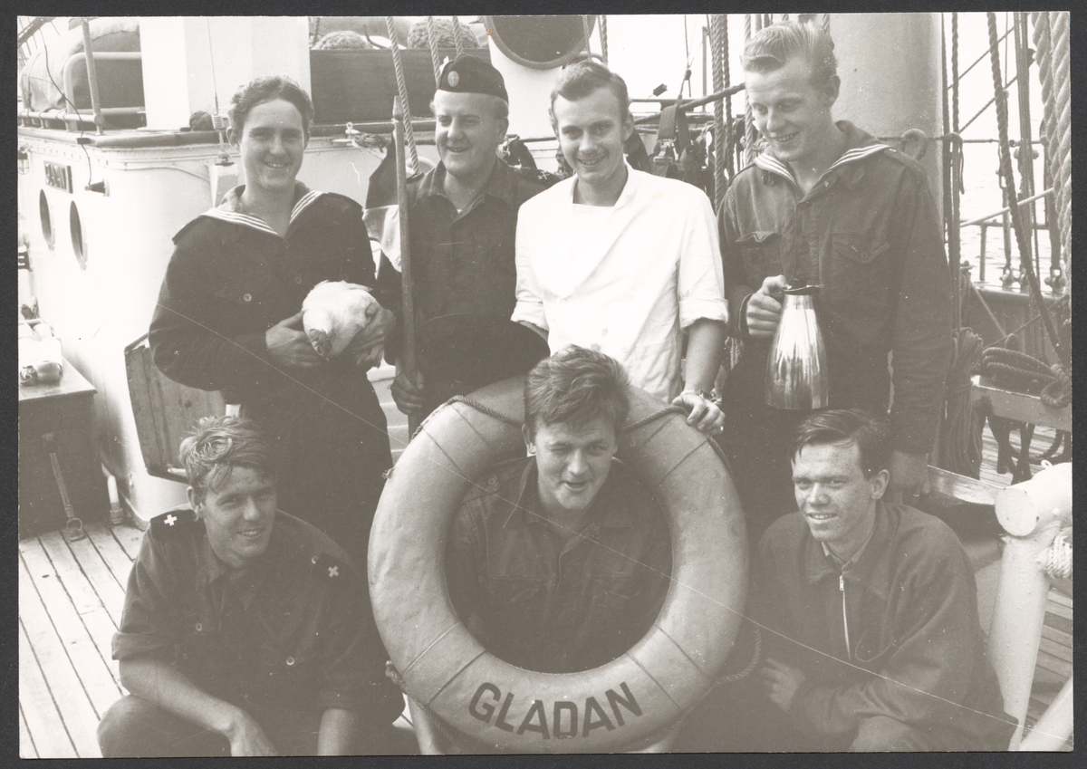 Grupporträtt av Gladans nyckelbesättning sommaren 1968 ombord på skolskeppet. Sjömännen bär olika prydnadssaker som en frälsarkrans, ett höns och en kaffekanna.