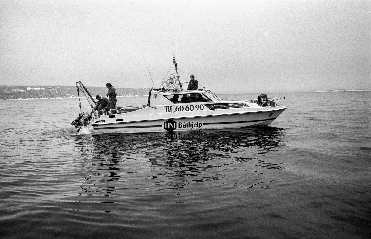 Miniubåtjakt etter dumpede biler og motorsykler i Oslofjorden utenfor Oppegård. Menn i kjeledress og strikkeluer håndterer miniubåten fra større båt, cabincruiser.