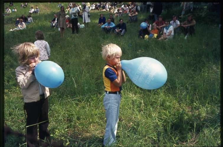 75-årsminnet av Andrées Nordpolsfärd firas med Ballongdagen på Åsavallen i Gränna 1972. Några barn blåser upp blå ballonger. På slänterna sitter publiken. Diabild.