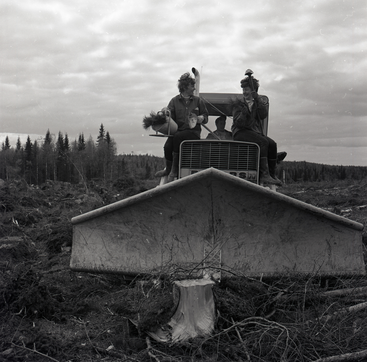 Två kinnor sitter på en skogsplog, 1969. I händerna håller de diverse redskap.