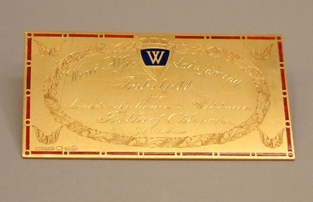 Fribiljett formad som plakett i guld, tilldelad Frithiof Ohlsson VD vid Wäxjö-Alvesta järnväg 1890-1909 vid hans avgång.
Plaketten ligger i ett blått etui.
Ingraverad text framsida, Wexiö-Alfvestads  järnväg, Fribiljett för Landssekreteraren o. Riddaren Frithiof Ohlsson, Styrelsen.
Text på baksida, Fribiljetten gäller äfven å Karlskrona-Wexiö, Wexiö-Klafreström- Åsheda och Wexiö-Tingsryda järnvägar.
Inköpt av järnvägsmusei vänner enligt styrelsebeslut 1989-01-24.
Gåva till Järnvägsmuseet 2004-04 från Järnvägsmusei vänner genom dåvarande ordföranden Erik Sundström, Sandviken.