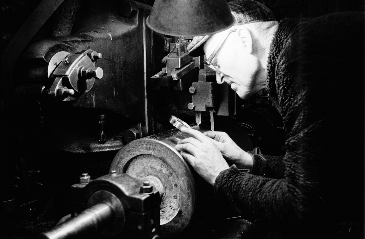 Fabrikör Karl-Gustav Johansson kontrollerar kvarnvalsens räfflor med hjälp av ett förstoringsglas, Enköpings Kvarnstensfabrik, Bangårdsgatan 13, Enköping, Uppland 1984