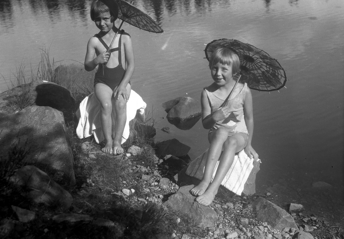 To jenter i badedrakter med parasoller på strand.