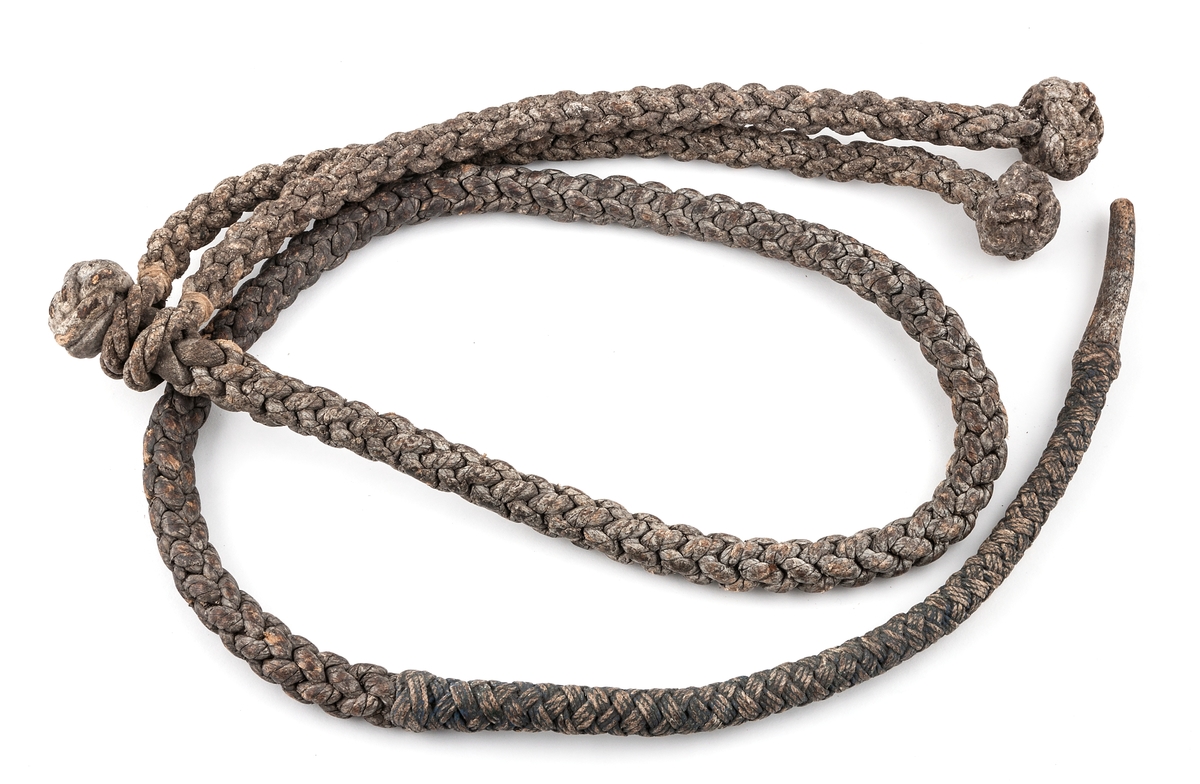 Knutpiska, flätad av skinn, består av en längd med knut i ena änden samt därinnanför fästade rörligt två kortare längder med knut.
Längd 1,55 m.