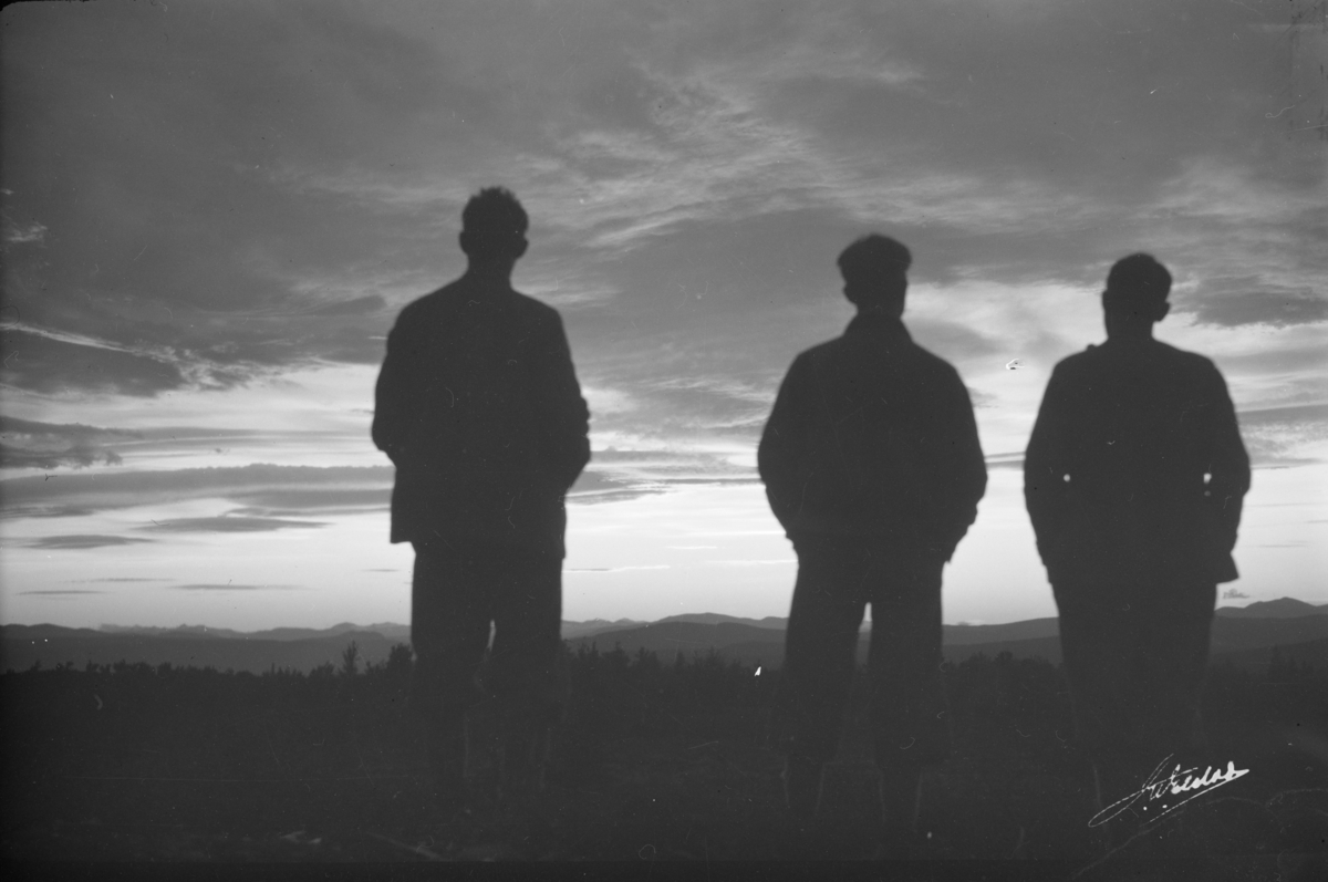Ringebu. Tre menn i siluett betrakter Jotunheimen ved solnedgang.