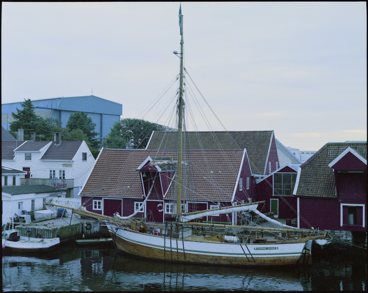 Hardagnerjakta "Johanne Karine" ved kai utenfor sjøhusene til Stiftelsen Haugesjøen på Kortaneset på Risøy, Haugesund. I bakgrunnen ligger det blå verftsbygget til H.M.V.