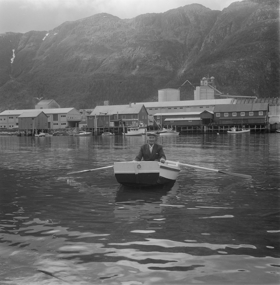 Småbåthavna i Mosjøen. Mann som ror pramme.
I bakgrunnen Flokkmannkaia og Aluminiumsverket.