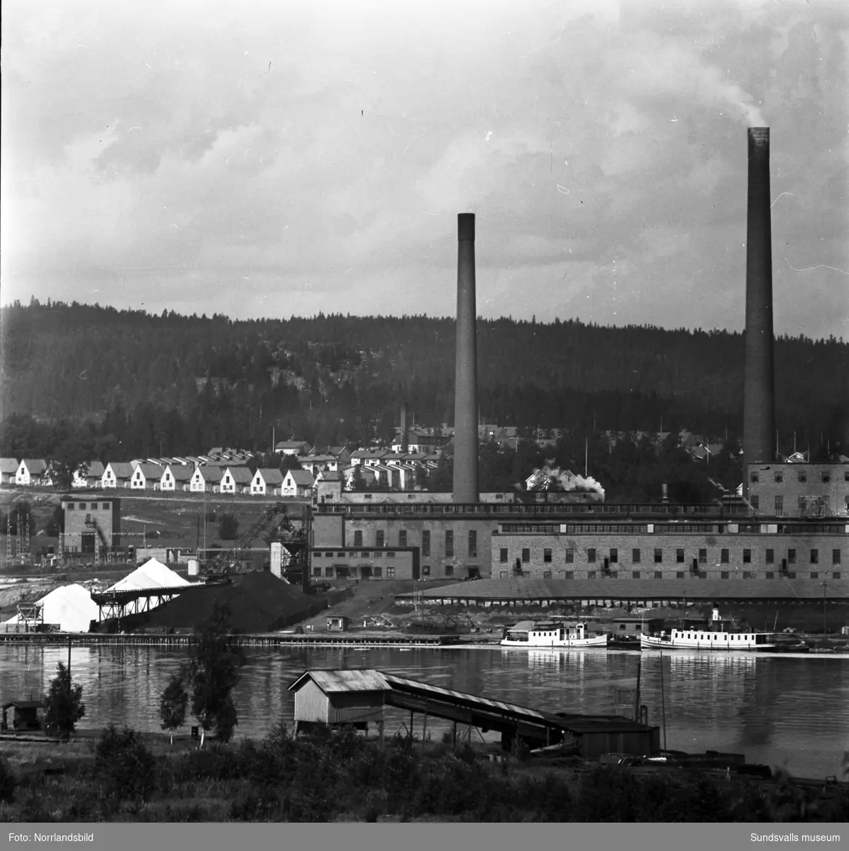 Östrandsfabriken och tjänstebostäderna på Näsberget fotograferat från Skönvik. Två pojkar poserar i förgrunden.