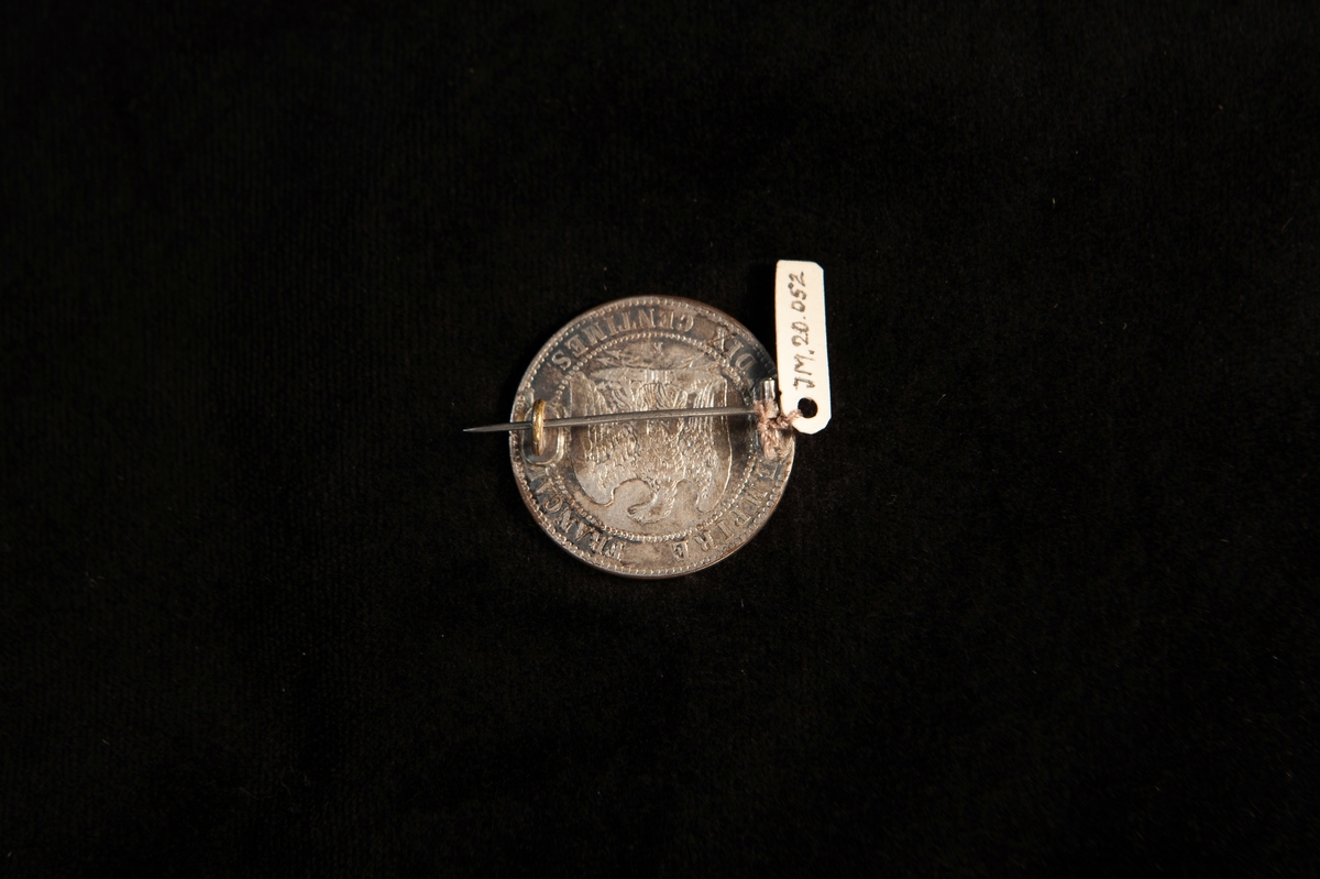 En rund brosch av silver i form av franskt mynt (10 centimes) från 1855.