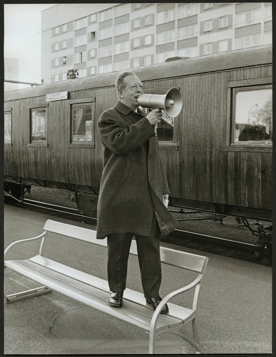 Framför personvagnen står en man med megafon på Centralstationen i Eskilstuna. Skylten på vagnen säger "Svenska Järnvägsklubben".