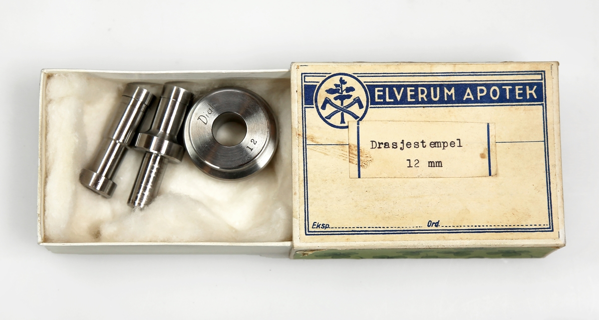 Etui av papp med logoen til Elverum apotek på framsiden og som inneholder deler til stempel (av metall), som trolig tilhører tablettmaskin