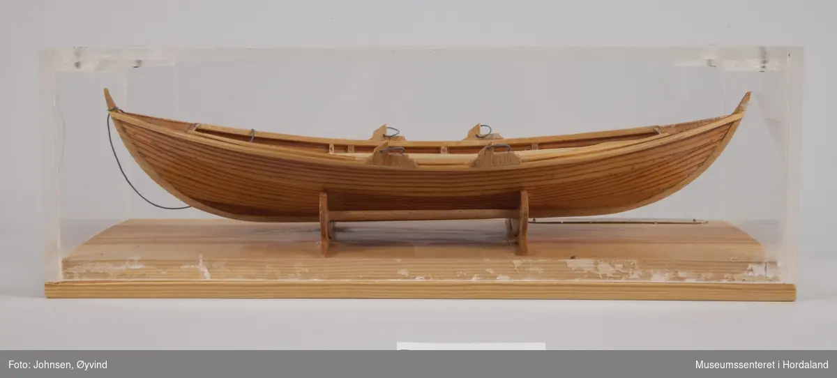 Båtmodell av Oselvar med to par årer. Satt i monter av pleksiglass og tre.