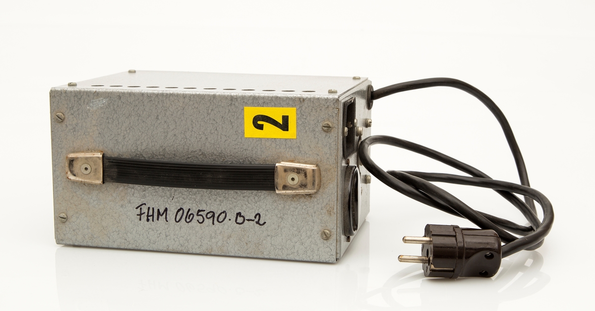 FHM.06590.b-1 Bell & Howell Sound Projector16mm filmframviser med integrert høyttaler. Dessuten FHM.06590.b-2 transformator, FHM.06590.b-3 vidvinkellinse i futteral, FHM.06590.b-4 metallholder til linse, FHM.06590.b-5 strømkabel til framviser, FHM.06590.b-6 stor filmspole, FHM.06590.b-7 liten filmspole.