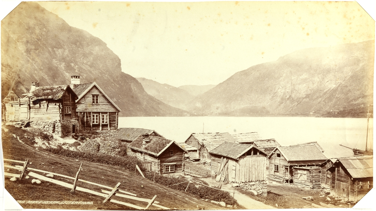 Marifjøra, Luster i Sogn. Gårdstun med mange uthus og naust. Fjord- og fjellandskap i bakgrunnen. Seilbåt ankret opp på fjorden. Fotografert mellom 1870 og 1886.