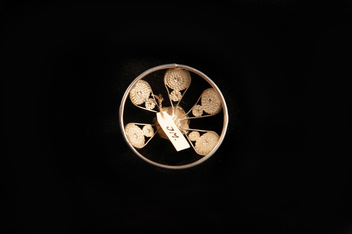 En malja av silver. Filigranarbete i form av fem st. "tungor" upp mot blomma i filigran. Stämplad på rundelns kant. JM.19973:a-e hör ihop.