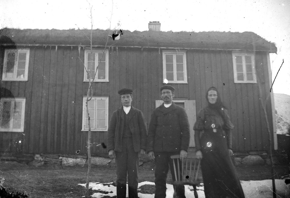 Leirfjord. Tre personer fotografert foran et hus, snø på bakken.