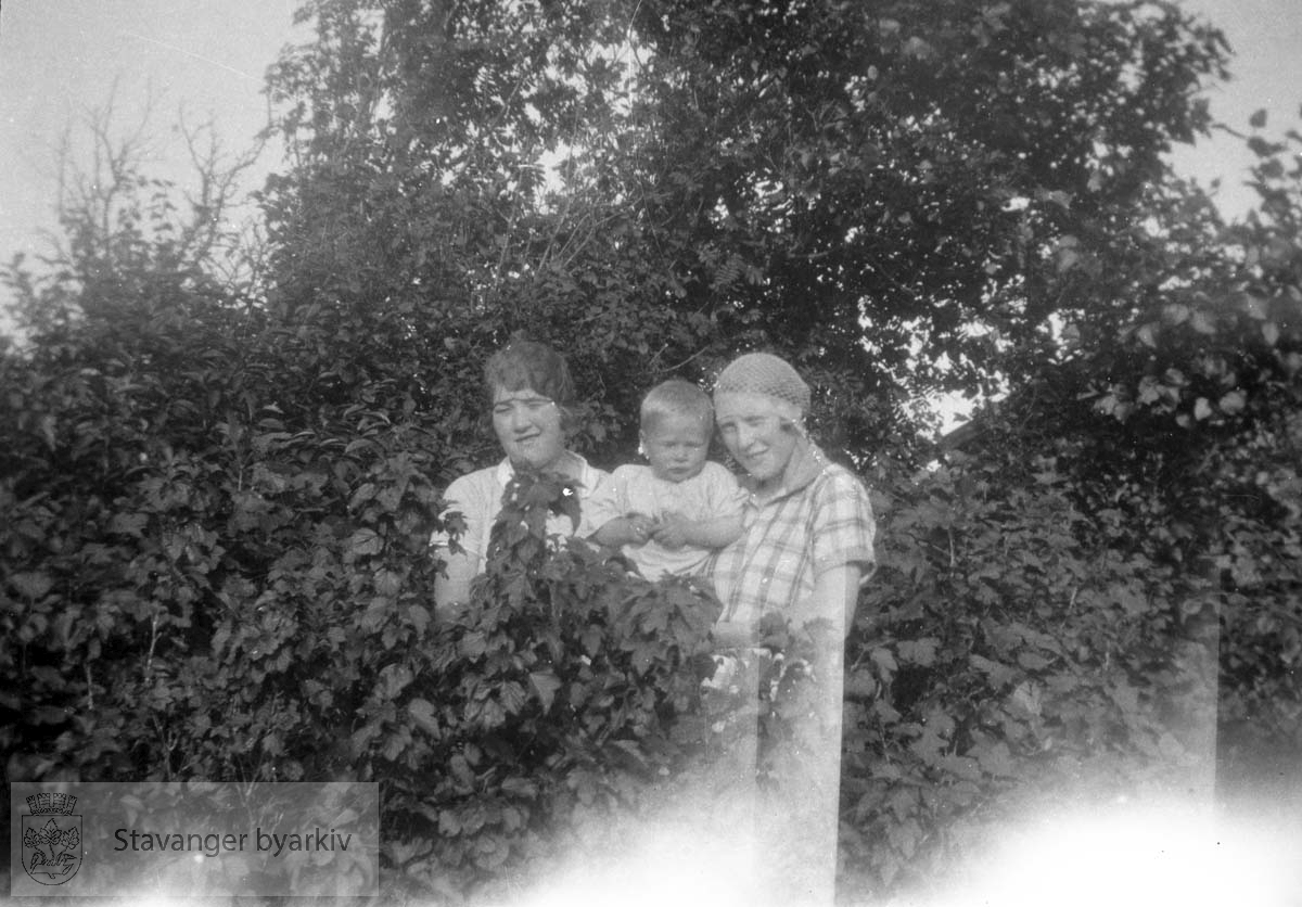 To kvinner og et barn i hagen blant busker