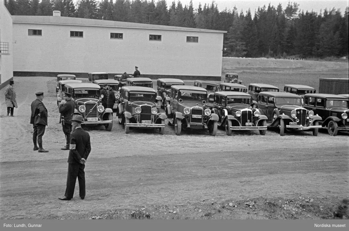 Invigning av Lovö vattenverk på Lovön i maj år 1933, chaufförer står vid parkerade bilar utanför vattenverket, närbild på en bil tillhörande Kungliga hovstallet.