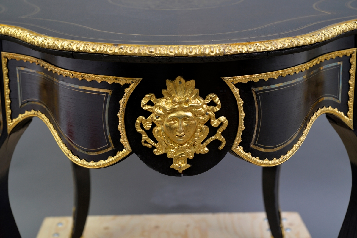 Ovalt bord (fransk), konstruksjon i heltre som er finert. Bordet har messing intarsia og pyntebeslag i metall. Overflate er antakeligvis malt med svart limfarge og lakkert.