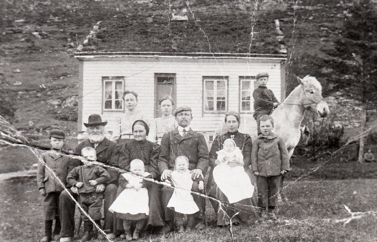 Gruppeportrett av en ukjent familie foran et hus. En gutt sitter på en hest.