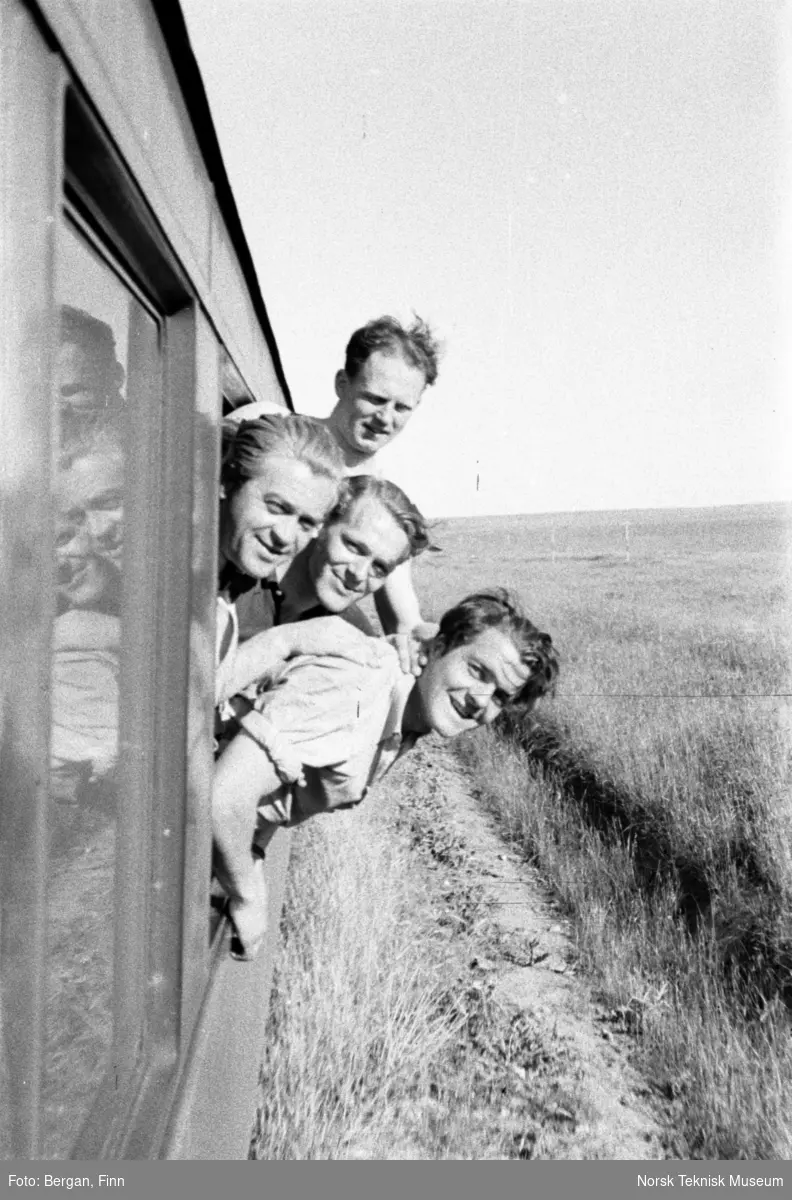 Fire person som lener seg ut av vinduet på et tog. Flatt landskap, strekningen Istanbul - Bagdad, Taurus Express.