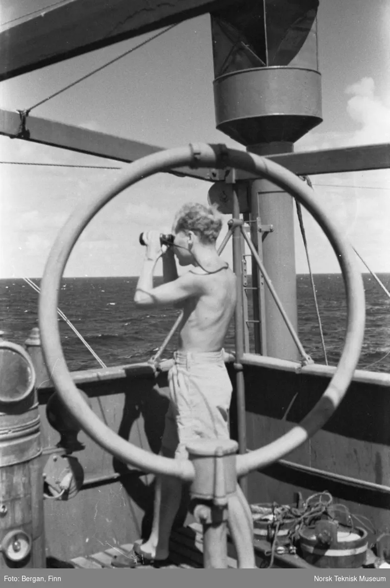 Person på skipsdekk, ser ut over havet med kikkert