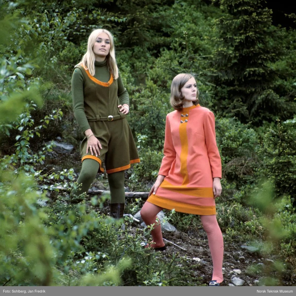 Motebilde, to kvinner poserer i skogen i klær fra kolleksjonen "Fjord Look", høsten 1968. Bildet er en del av en serie der noen er publisert i ukebladet Det Nye. Billedtekst: I forgrunnen ser du Joan i en ørretfarget kjole med høstfarget innfelling, både i stripe ned foran og som to striper nedentil. Stoffet er 90% ull og 10% nylonforsterkning. Prisen er ca kr. 156,-. Den morsomme ermeløse buksekjolen i "mose" med belte og høstfargede kantinger er vel midt i blinken denne sesongen. Stoffet er ull/ nylon og prisen er ca kr. 154,-."
