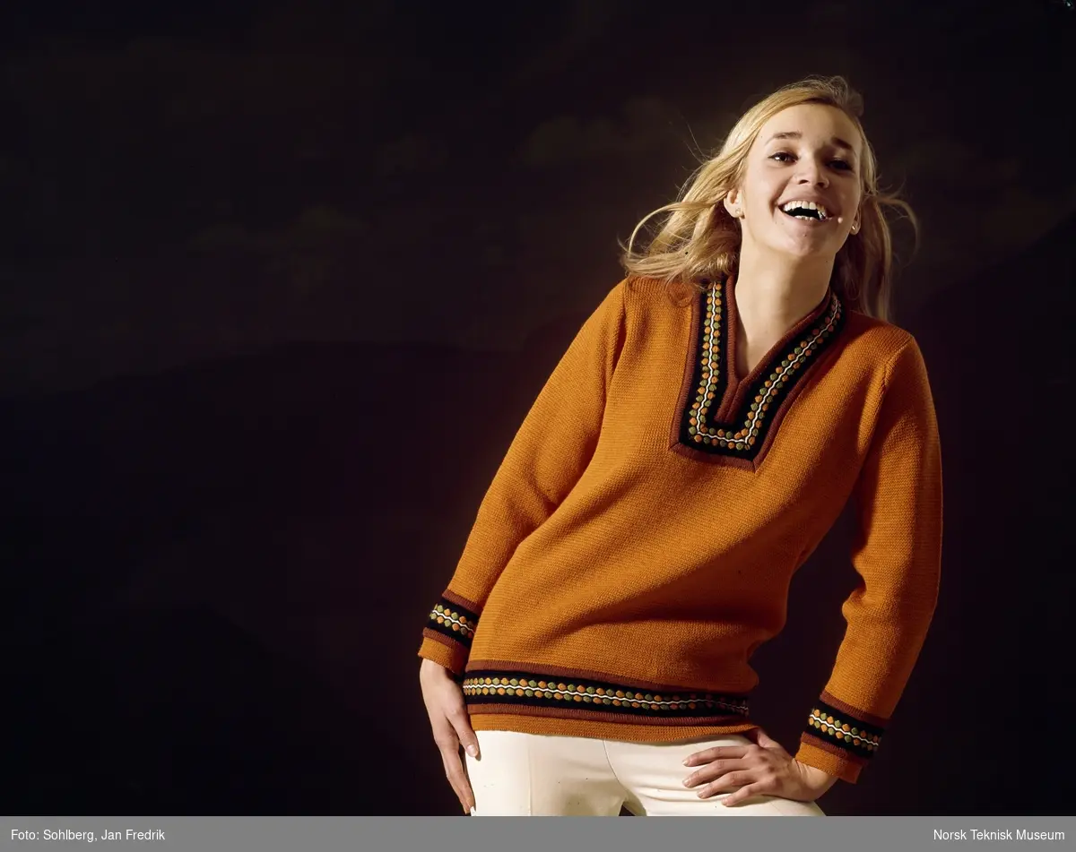 En kvinnelig modell viser fram en okerfarget strikkegenser. Studiofoto.
