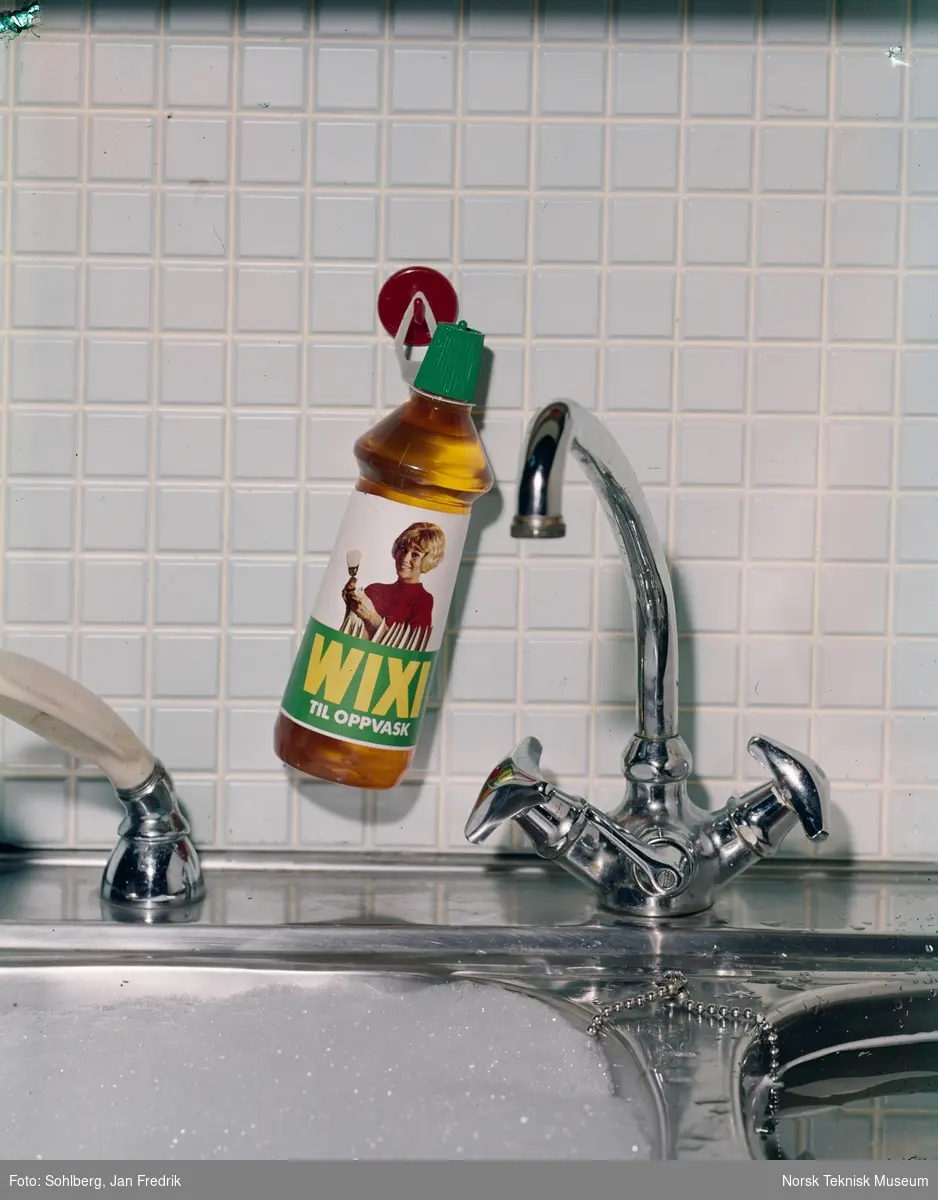 Reklamefoto for oppvaskmiddel av merket Wixi. En flaske med produktet henger over en oppvaskkum. Det er skum i kummen.