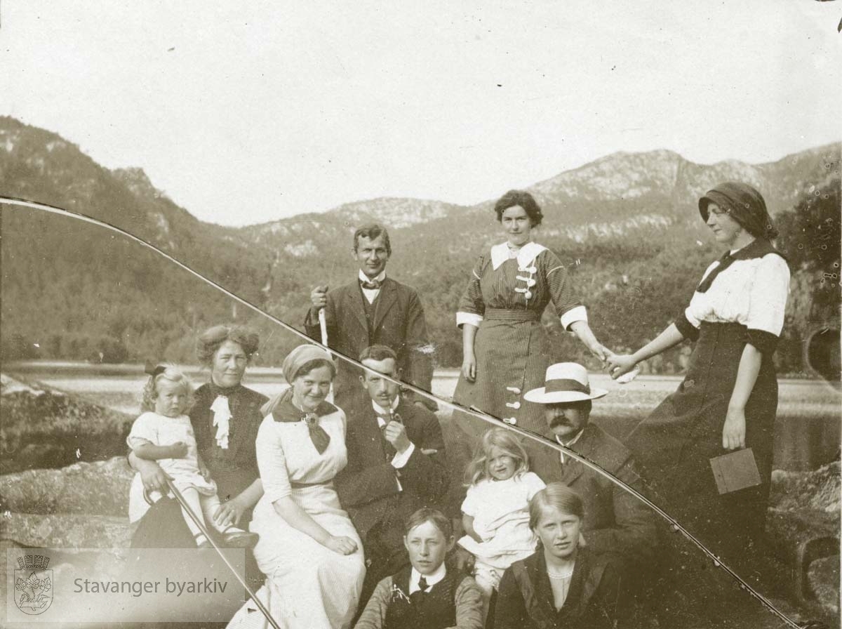 Voksne og barn poserer for fotografen med vann og fjell i bakgrunnen.
