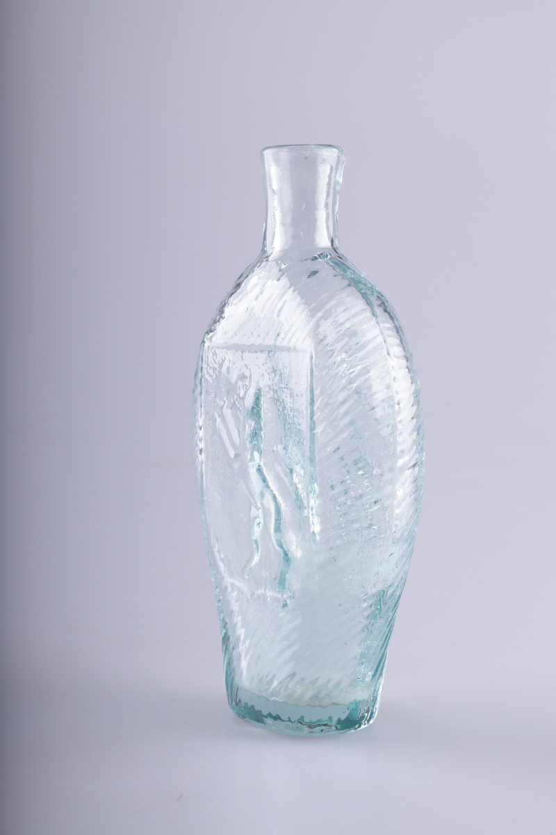 Flaske i grønnlig glass, blåst i form. Rommer en halv pegel. Motivet på den ene siden viser den norske løve, på den annen en drueklase.