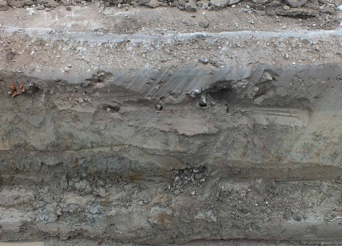 Arkeologisk schaktningsövervakning, täckdike med rundade stenar i botten i östra schaktväggen, Katedralskolan, Uppsala 2017