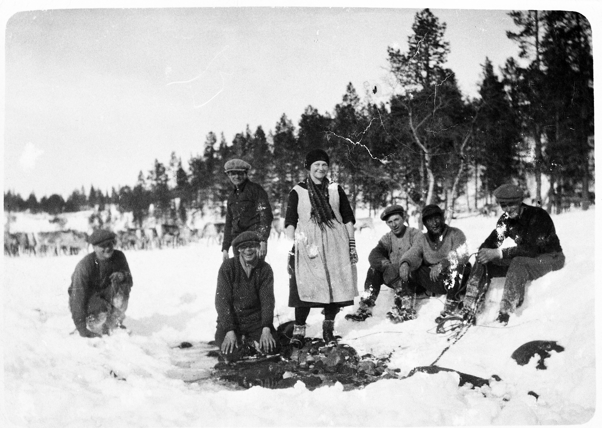 Sju personer avbildet ute i snøen. Reinflokk i bakgrunnen.