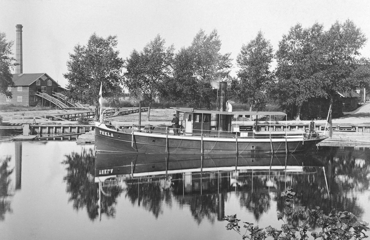 Motiv från Linköpings hamnområde 1892. Vid kaj ses bogserångfartyget Tekla, byggd i Stockholm 1889 för trafik på Kinda kanal. Fartyget tillhörde P. Wikström i Stockholm som även ägde Linköpings ångsåg vars anläggning ses till vänster.