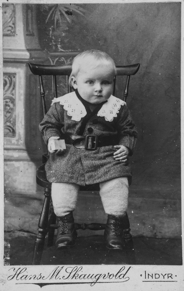 Leirfjord, Simsø. Barneportrett av Hans Hansen fra Simsø (f. 1913). Han sitter på en stol og  er kledd i fin jakke/kjole med krage og belte i livet. På føttene har han små skinnsktøvler. 
Bildet er brukt i Leirfjordkalenderen - november 2017