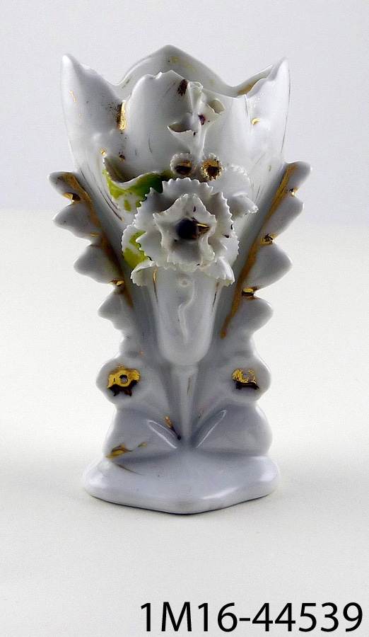 Vas av porslin, med blommor (varav troligen en nejlika) och blad på framsidan, detaljer målade i grönt och guld. Vasen är något skadad.
