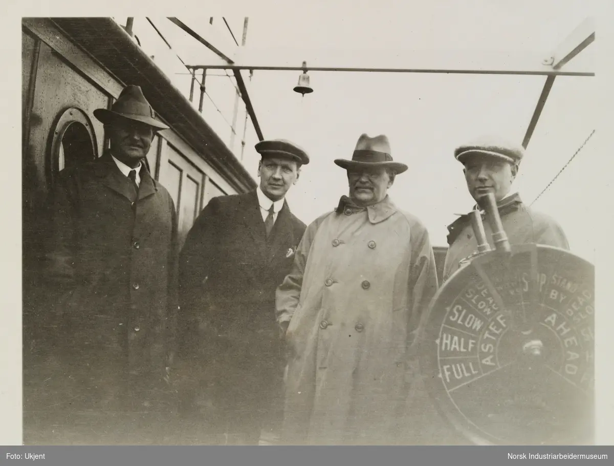 Fire menn med hatter står på kommandobroen ved maskintelegraf