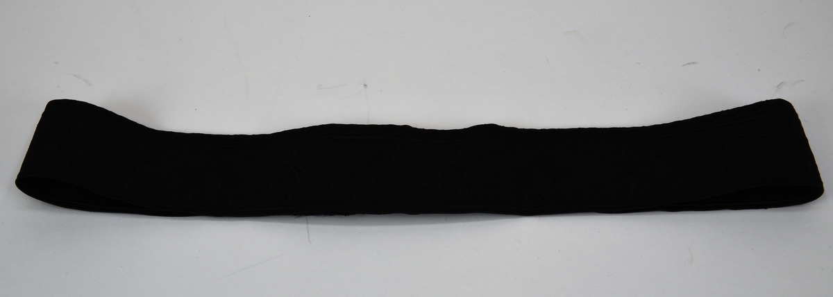Ett mössband av svart mönstervävt tyg som fästs med kardborreband. Mönstret består av SJ:s bevingade hjul samt SJ:s logotyp i upprepande mönster.