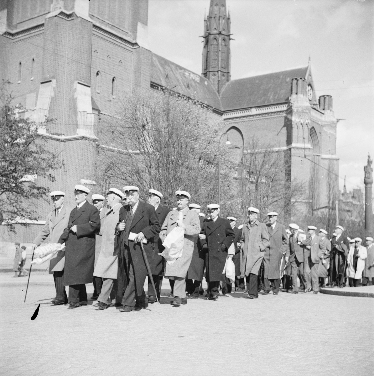 Flera personer iförda studentmössor tågar tillsammans längs Biskopsgatan, Östgöta nations minneslandskap, Uppsala 1949