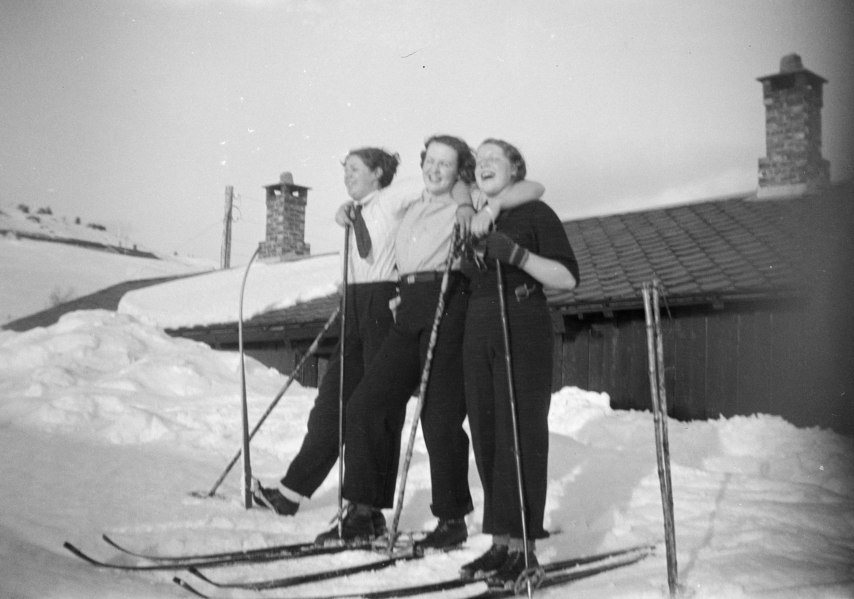 Tre kvinner på ski fremfor en hytte