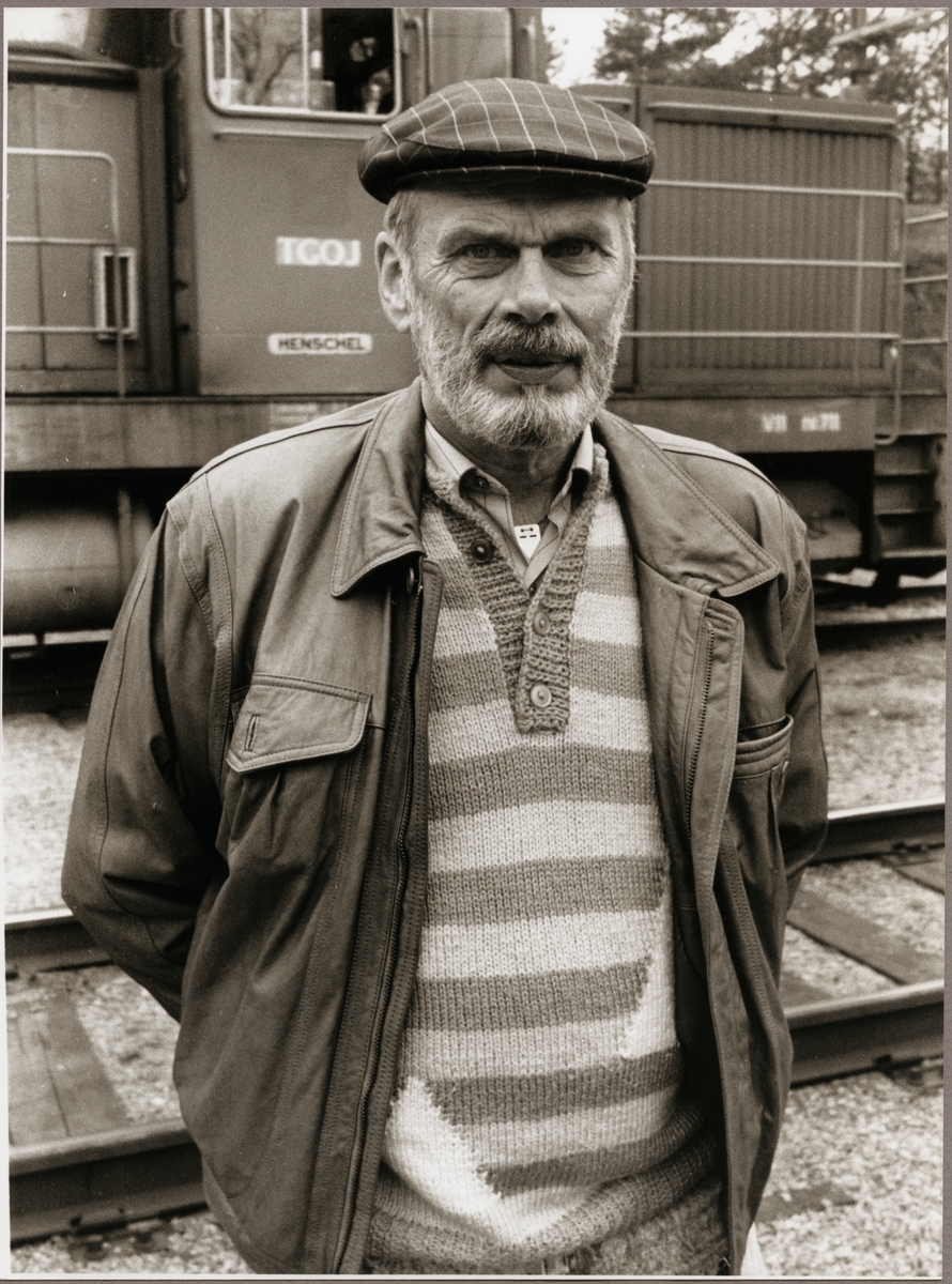 Karl-Erik Svedlindh pensionerad lokförare vid Trafikaktiebolaget Grängesberg - Oxelösunds Järnvägar, TGOJ i Oxelösund. Bakom honom står TGOJ V11 711.