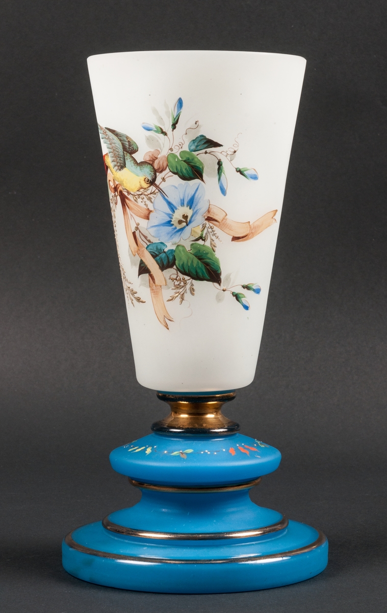 Vas av flussat glas, foten blå med guldränder, på själva vasen målning med blommor och en fågelbild.