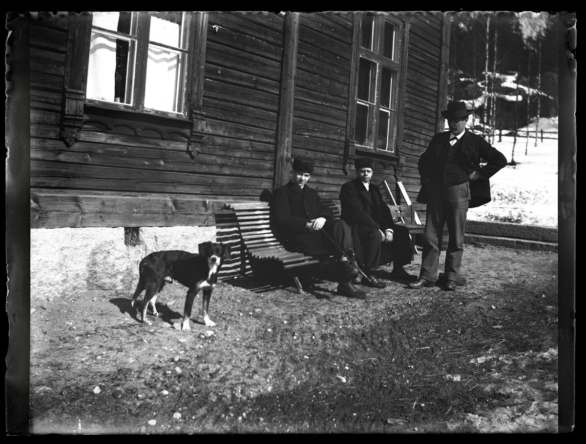 Tre män på/vid en bänk och en hund, Riddarhyttan.
