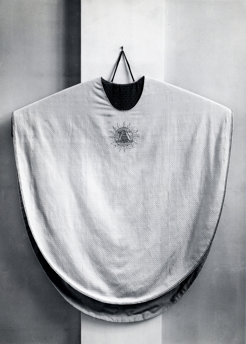 Foto (svart/vitt) av en ljus mässhake (framsidan ?) med mörkare broderat parti, med monogram "A", omgivet av solstrålar.
Beställd av Karlskrona Amiralitetsförsamling. 

Inskrivet i huvudbok 1983.