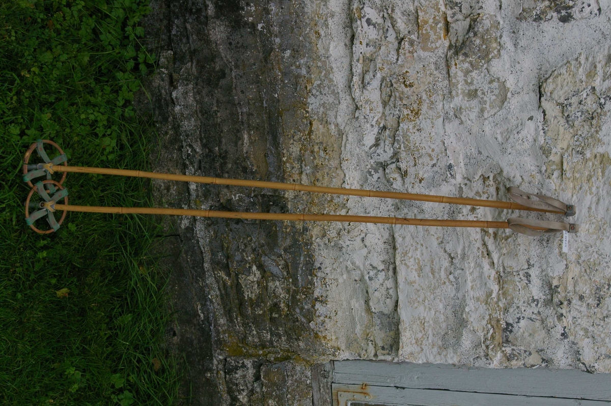 Et par skistaver av bambus med håndtak av skinn, og trinser med pigger nederst.