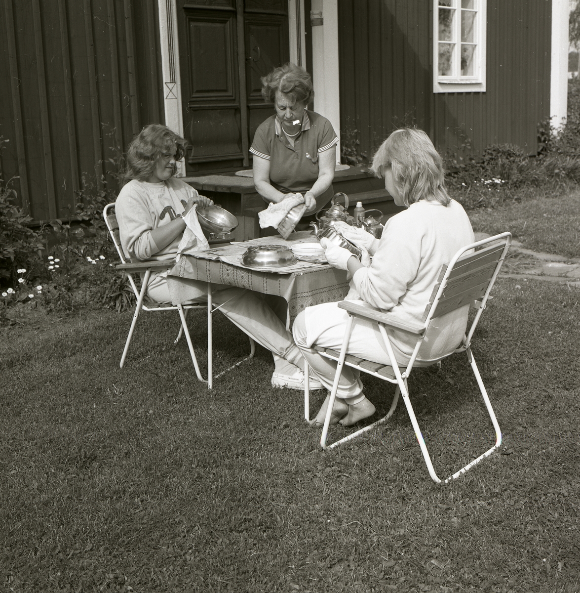 Tre kvinnor putsar skålar och kakformar vid ett bord hemma hos Hilding Mickelsson, juni 1986.