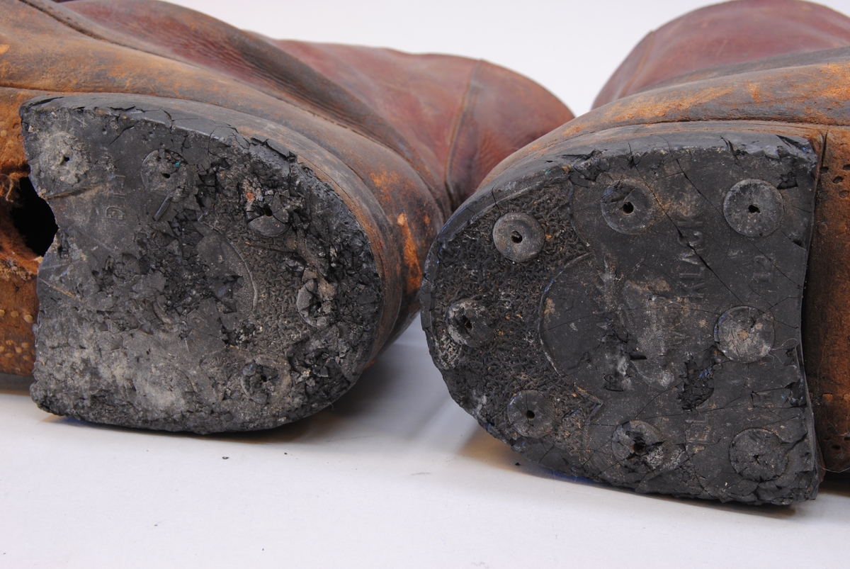 Bruna läderkängor med högt skaft. Kängorna har mässingsöljetter och lädersnören. Under klacken står det "ELG".