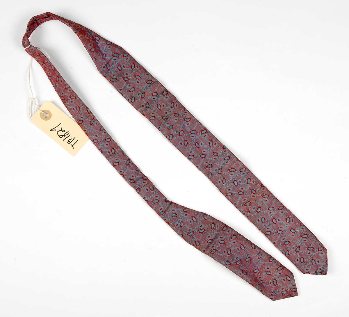 Mønstrete slips med brede stykker i hver ende, det ene lengre enn det andre. Spiss i begge ender. Fòret med annet stoff.