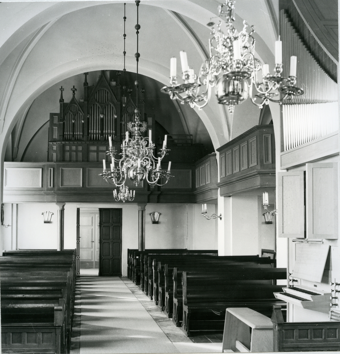 Lundby sn.
Lundby kyrka, interiör med kyrkbänkar, kyrkorgel och malmkronor. 1975.