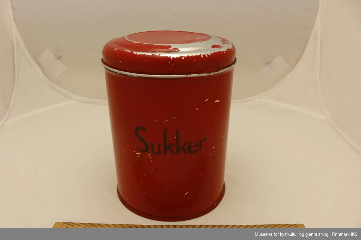 rød, rund blikkboks med lokk med ordet "sukker" skrevet på siden. Det er skrevet "NO 199" på undersiden av boksen og på innsiden av lokket.